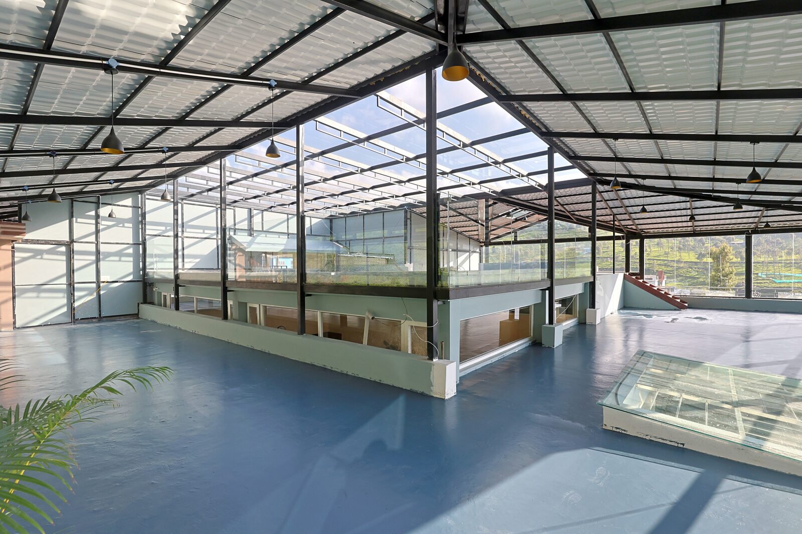 The banquet hall at Sinnis Home Stay — a glass-walled pavilion under a steel roof with tea slopes visible on every side