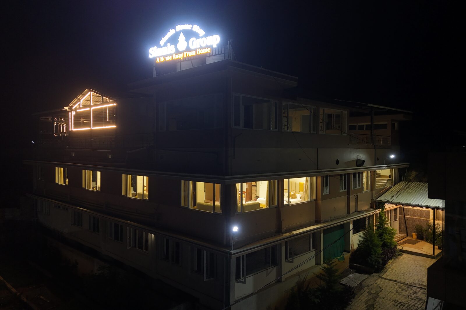 Sinnis Home Stay lit up at night with the illuminated rooftop sign above the hillside